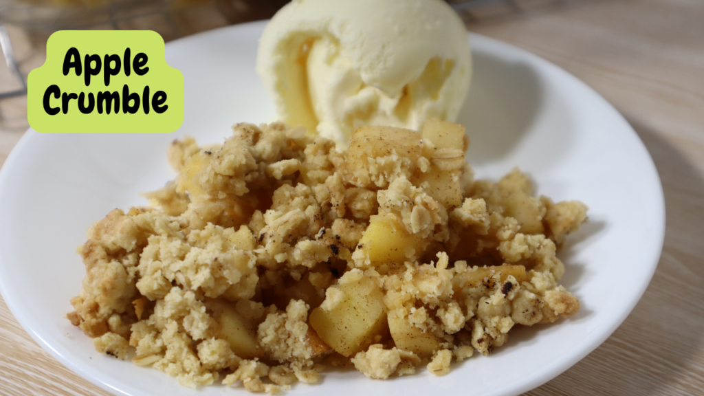 A plate of Apple Crumble with a scoop of vanilla ice cream. Top left corner says Apple Crumble in a yellow background.