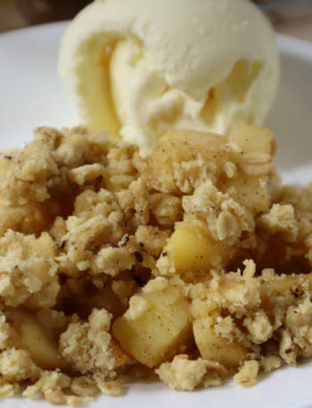 A plate of Apple Crumble with a scoop of vanilla ice cream. Top left corner says Apple Crumble in a yellow background.