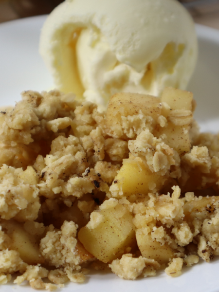 A plate of Apple Crumble with a scoop of vanilla ice cream. Top left corner says Apple Crumble in a yellow background.