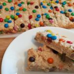 2 peices of M&M slice on awhite side plate with M&M slice in the background