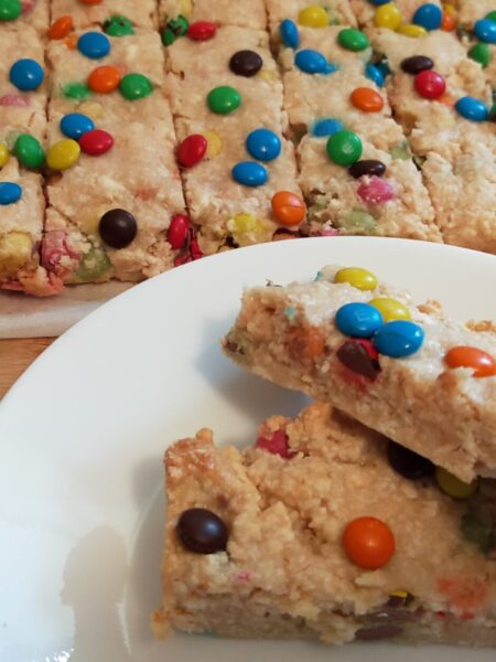 2 peices of M&M slice on awhite side plate with M&M slice in the background