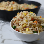 Bowl with fried rice at the front and frying pan with fried rice blurred at the back.