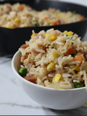 Bowl with fried rice at the front and frying pan with fried rice blurred at the back.