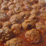 Aluminum tray with cooked meatballs in a tomato sauce. Above head angle shot.