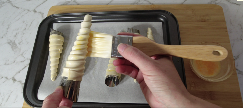 Brushing egg yolk on puff pastry cream horns