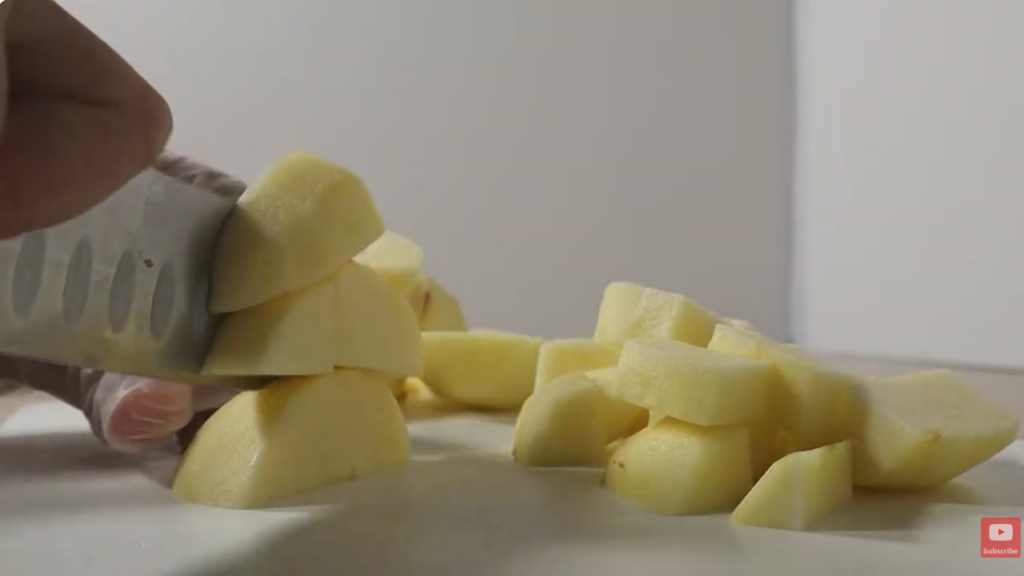 White chopping mat with a knife about to cut apples in bite size peices. Pre-cut apple in the background