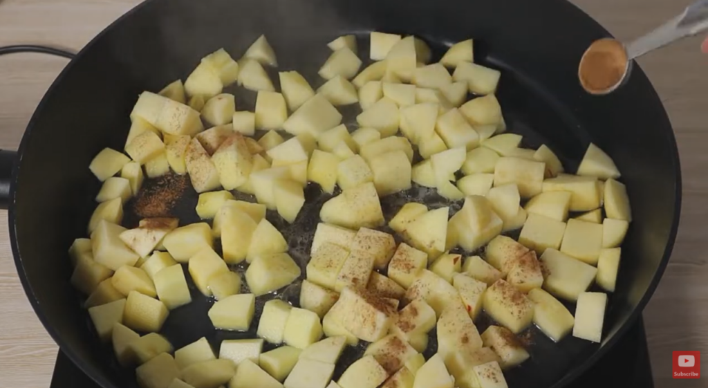 Frying pan cooking diced apples while hand-pouring cinnamon over the top.