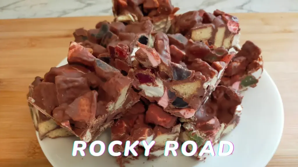 Pieces of homemade Rocky Road on a white board with chocolate, lollies and marshmallows visible