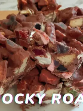 Pieces of homemade Rocky Road on a white board with chocolate, lollies and marshmallows visible