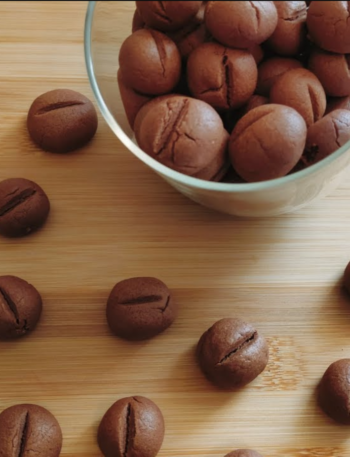 Coffee Bean Shaped Cookies in a jar with some scattered around the bench
