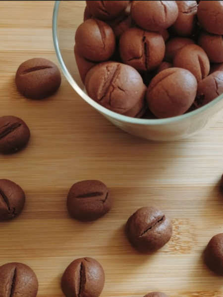 Coffee Bean Shaped Cookies in a jar with some scattered around the bench