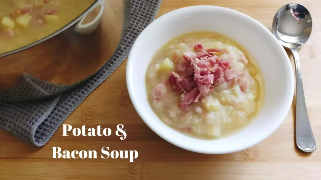 Bowl of Potato and Bacon soup with a soup spoon to the right and a pot of Potato and Bacon soup on the back left side.