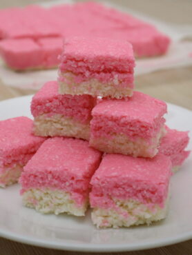 Pink and white coconut ice squares stacked on a plate
