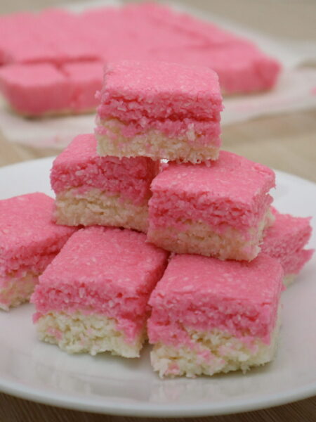 Pink and white coconut ice squares stacked on a plate