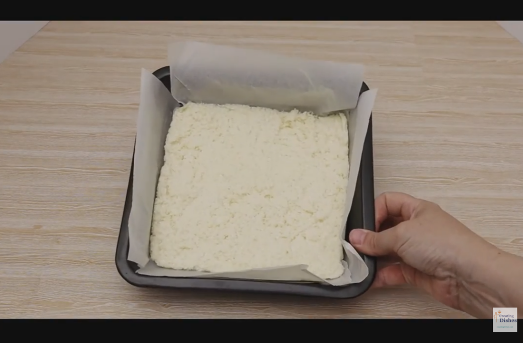 Lined baking tin with white coconut ice mixture in the base.