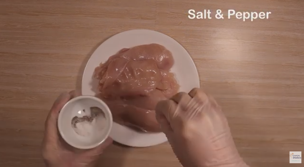 Salt and Pepper being sprinkled over the chicken breast, cut in half lengthwise. 