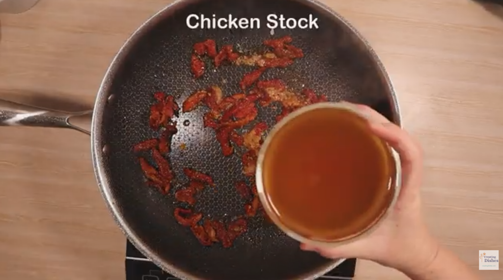 Frying pan with sundried tomato strips, garli, tomato paste and my hand holding chicken stock.