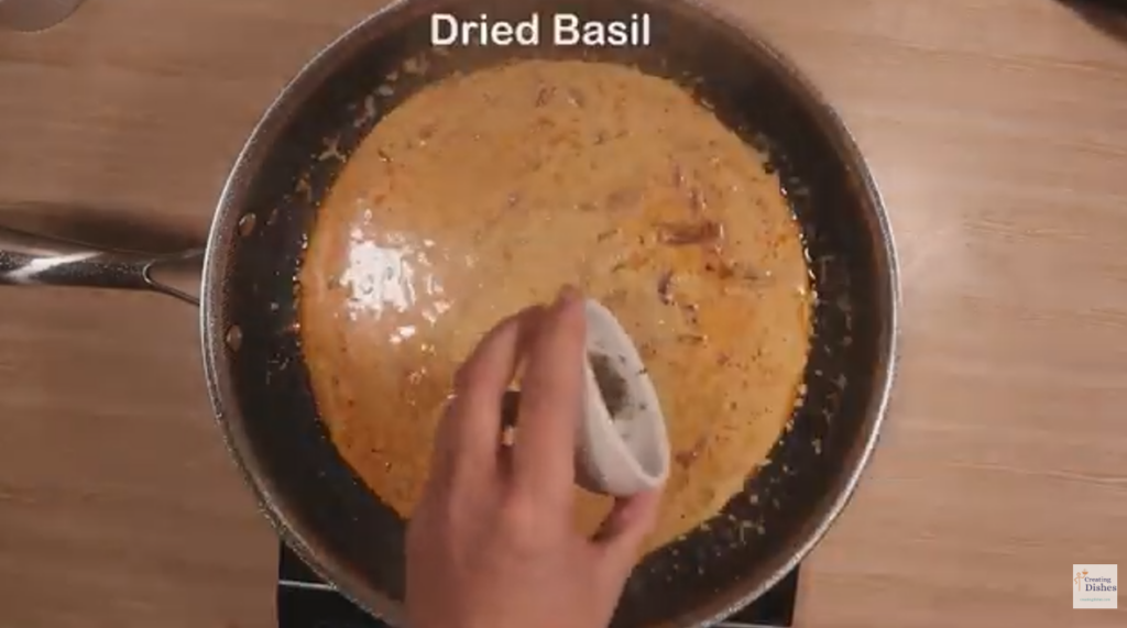 Frying pan with Marry Me Chicken sauce cooking, adding dried basil to the sauce