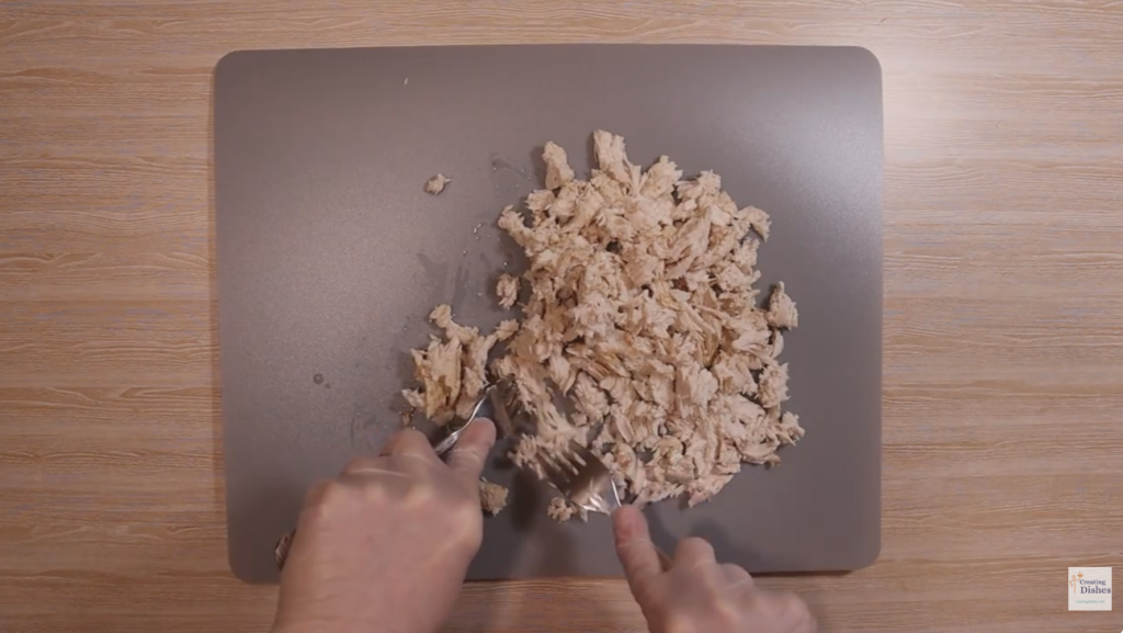 Cooked chicken is being shredded using forks