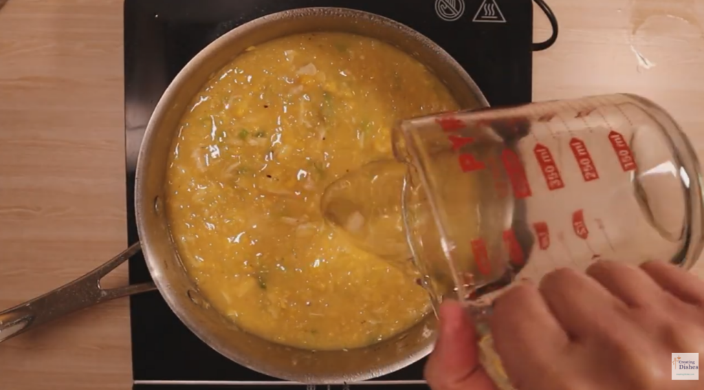 Adding chicken stock and water to the chicken and sweet corn soup in the saucepan
