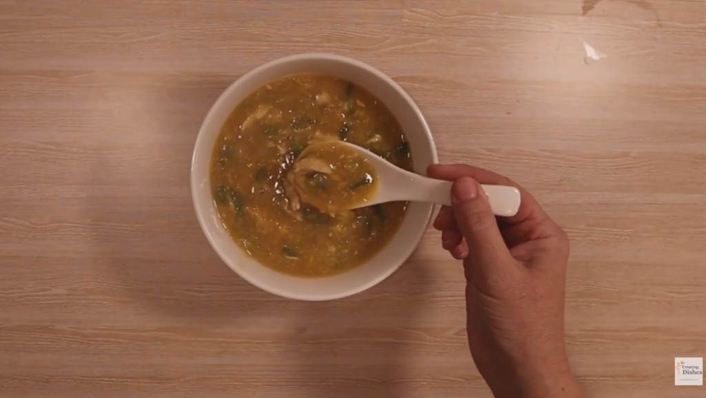 Bowl of chicken and sweet corn soup with a Chinese spoon being held with soup on it.