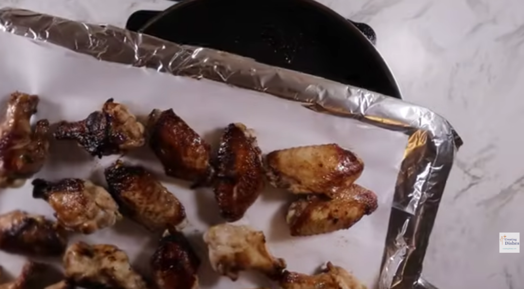 Lined oven tray with browned chicken wings going in the oven