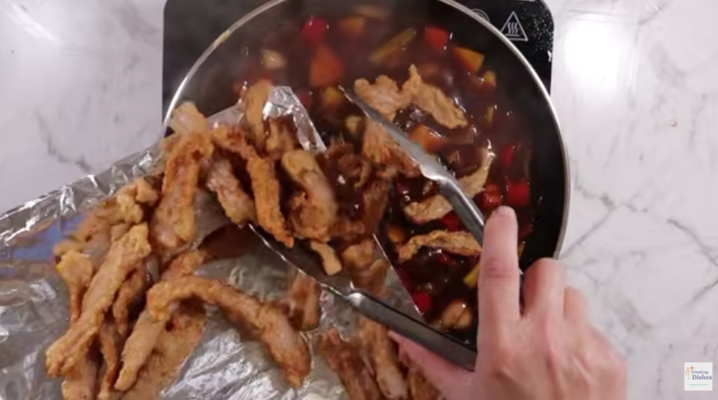 Adding crispy cooked pork to the sweet and sour sauce